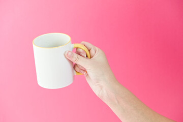 Woman's hamd holding coffee, tea ceramic cup on a pink background. White mug in the frame. Isolated...