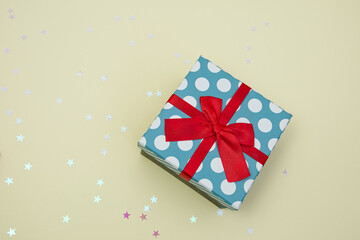 Obraz premium Gift box decorated with bright red knotted bow and dotted wrapping paper, ribbon, glitter decorative stars. Present, celebration, anniversary concept composition. 