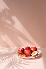 Sweet delicious summer fruits, plate with nectarines or peaches on peachy pink background with aesthetic floral sunlight shadows, healthy vitamin organic food for diet and detox, empty copy space