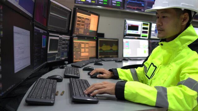 Engineer working in a control room,programming to manage industrial machines,monitoring multiple screens,efficient workflow