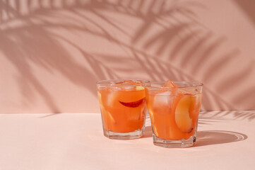 Fresh delicious summer iced fruit drinks, peach soft cocktails in glasses on vibrant peach color background with palm foliage sun light shadows, empty copy space