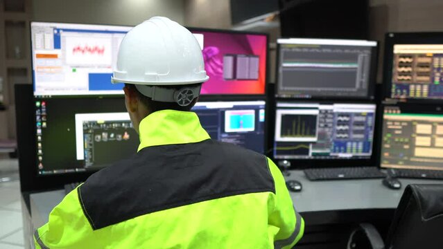 Engineer working in a control room,programming to manage industrial machines,monitoring multiple screens,efficient workflow