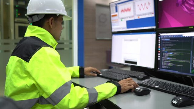 Engineer working in a control room,programming to manage industrial machines,monitoring multiple screens,efficient workflow