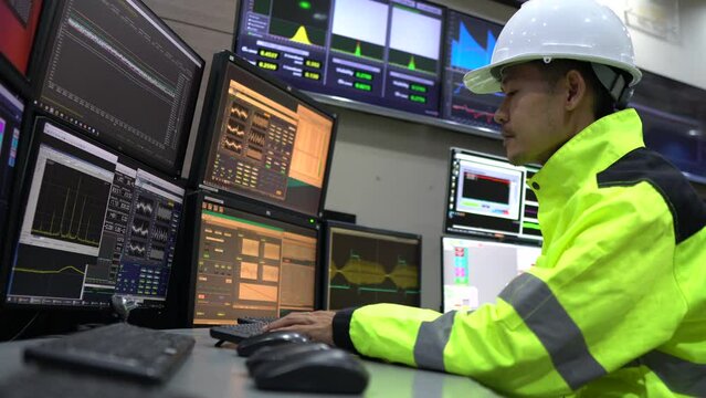 Engineer working in a control room,programming to manage industrial machines,monitoring multiple screens,efficient workflow