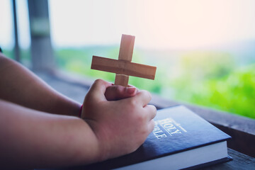 Close up hands child girl holding cross praying on bible, christian concept.