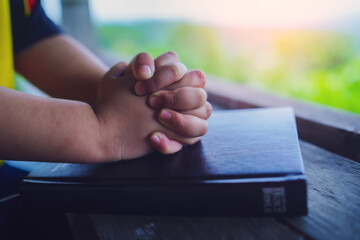 Close up hands of child girl praying on bible in morning, christian concept.