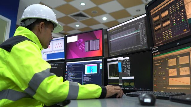 Engineer working in a control room,programming to manage industrial machines,monitoring multiple screens,efficient workflow