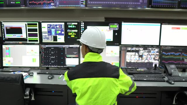 Engineer working in a control room,programming to manage industrial machines,monitoring multiple screens,efficient workflow
