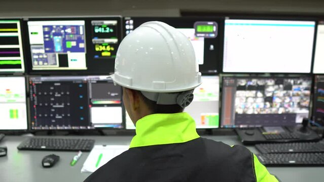 Engineer working in a control room,programming to manage industrial machines,monitoring multiple screens,efficient workflow