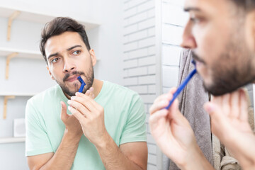 Handsome man looking at the mirror and shaving in the bathroom	