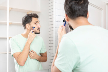 Handsome man looking at the mirror and shaving in the bathroom	