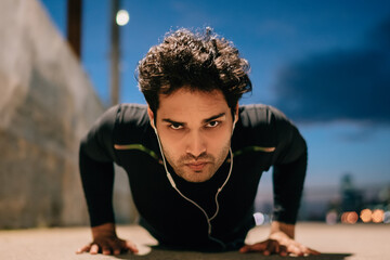 Portrait of young athlete man dressed in active wear for training push up from ground and looking...