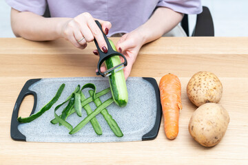 Close-up shot of a woman peeling vegetables using special vegetable peelers in the kitchen	