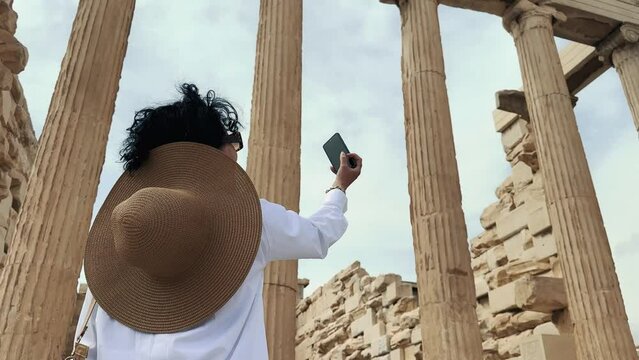 Hispanic curly hair fashion woman with hat is visiting Parthenon, Acropolis in ancient Athens, Greece