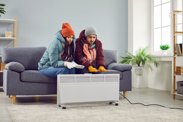 Full length photo of a young frozen couple sitting on the sofa in the living room in winter...