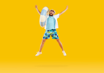 Cheerful male vacationer with inflatable beach circle jumping high on orange studio background....