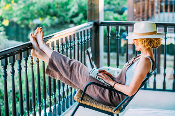 A woman is sitting on a rocking chair on a balcony, wearing a straw hat
