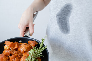 Dirty grease stain on clothes. An unrecognizable person a frying pan with meat and herb. Cooking in...