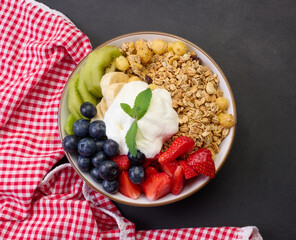 Healthy breakfast. Granola with strawberries, kiwi, banana and blueberries in a round plate on a black table.