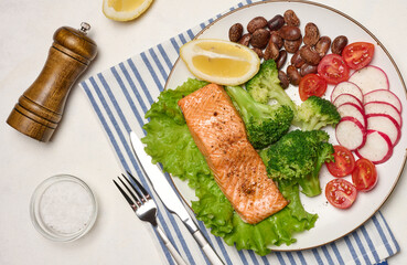 Healthy lunch with grilled salmon on green lettuce, next to vegetables, tomatoes, radishes, broccoli and a portion of beans.