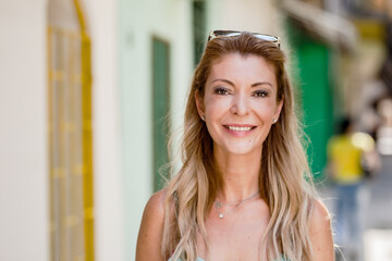 Middle-aged Caucasian woman smiling confidently on a sunny street, exuding happiness and...