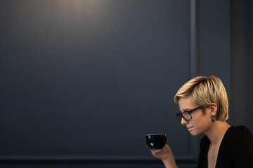 A thoughtful businesswoman enjoys a cup of coffee in a serene office setting, reflecting a moment...