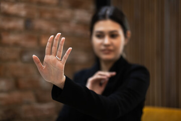 A focused Asian businesswoman in a black suit making a stop gesture in a modern office setting, conveying boundaries and assertiveness.