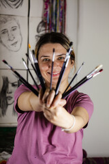 Artistic girl holding many dirty colorful used brushes with both hands.