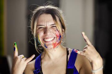 A female artist expressing joy and creativity, covered in vibrant paint, laughing with paint on her hands and face in her studio.