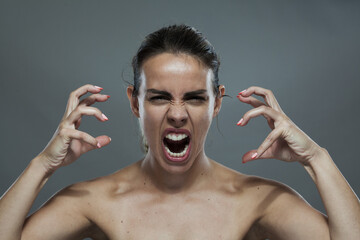 Intense woman making a fierce expression with hands like claws against a gray background