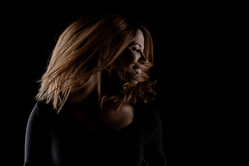 Naklejka premium Stunning low key image of a young woman captured in mid-motion, highlighting the graceful flow of her hair against a dark backdrop.