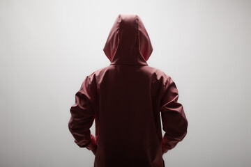 Mysterious young woman in maroon hoodie facing away on plain background