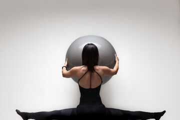 Young woman practicing yoga with a fitness ball in a serene white studio