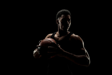 Basketball player holding a ball against black background. Serious concentrated african american man.
