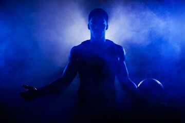 Basketball player holding a ball against blue fog background. Muscular african american man...