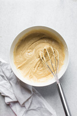 Overhead view of vanilla cake batter being whisked in a white ceramic bowl, flatlay of cake batter being mixed, process of making cake