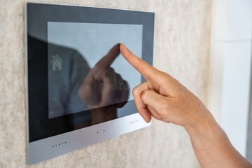 View of hand of man using tablet panel application for control smart home living. Wireless device controller for home automation IoT on the wall