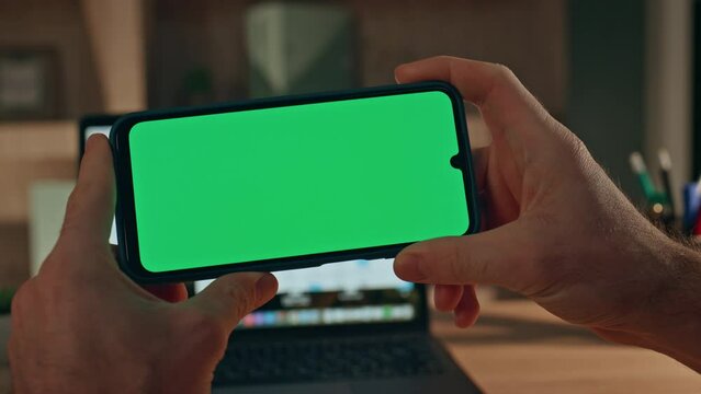 Unknown man watching green screen smartphone video in evening home close up.