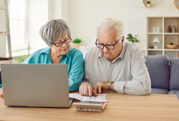 Senior couple sitting at the table with laptop looking at the bills calculating finances or taxes...