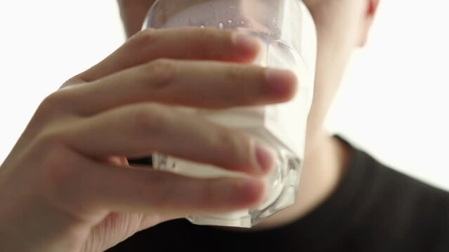 a man drinks milk from a transparent glass.
The guy drinks kefir and wipes his face