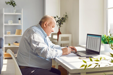 Old senior man working using laptop with chart sitting at the desk at home. Elderly retired person...