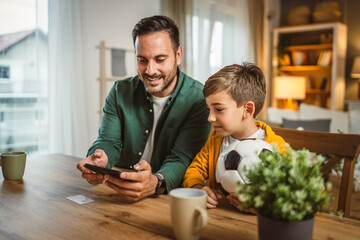 Father and son watch football match on mobile phone and cheer at home