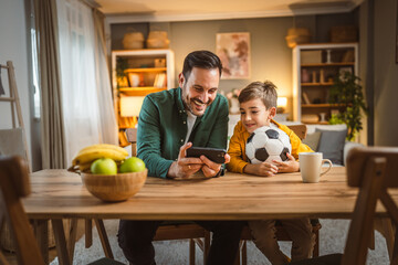 Father and son watch football match on mobile phone and cheer at home © Miljan Živković