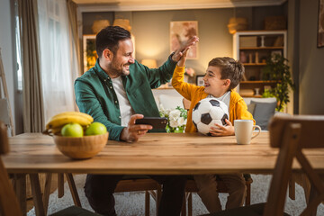 Father and son watch football match on mobile phone and cheer at home