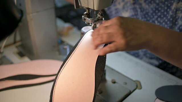 Male shoemaker works on sewing machine at the private workshop. Male bootmaker is sewing fabrics for shoes in shoe workshop. Shoe making process