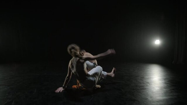 Group of a professional dancers are practicing capoeira in darkness against a spotlight on a black background of studio. Afro-Brazilian martial art that combine elements of dance.