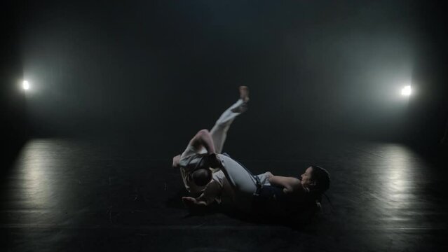 Group of a professional dancers are practicing capoeira in darkness against a spotlight on a black background of studio. Afro-Brazilian martial art that combine elements of dance.