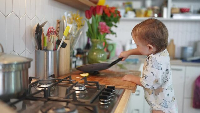 baby plays in the kitchen. happy family kid concept. baby son plays lifestyle in the kitchen with fireweed baby climbed onto a chair near the kitchen stove, plays with tongs dream, kitchen tools