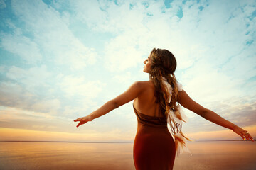 Carefree Girl looking away over Sunset Sea. Boho style Woman enjoying Sun and Tranquility Arms...