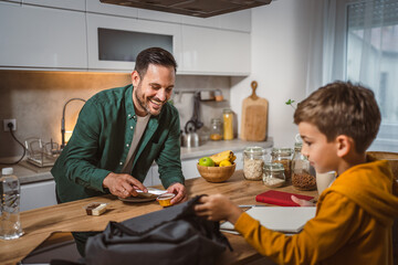 Dad prepare chocolate cream on bread while son pack backpack school